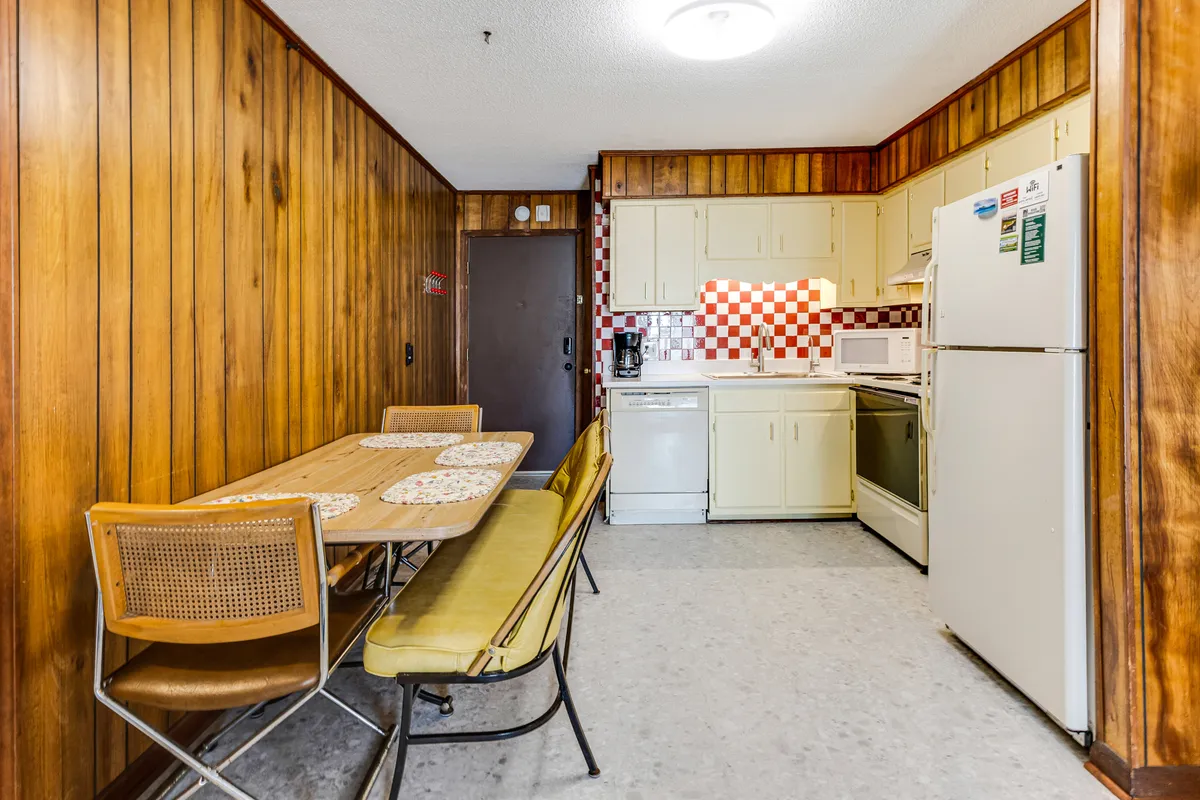 This image highlights a kitchenette with wood paneling, a checkered backsplash, a dining table, and kitchen appliances. The scene is set for casual meals, family recipes, and social gatherings, tying into the section's emphasis on easy living and shared moments.