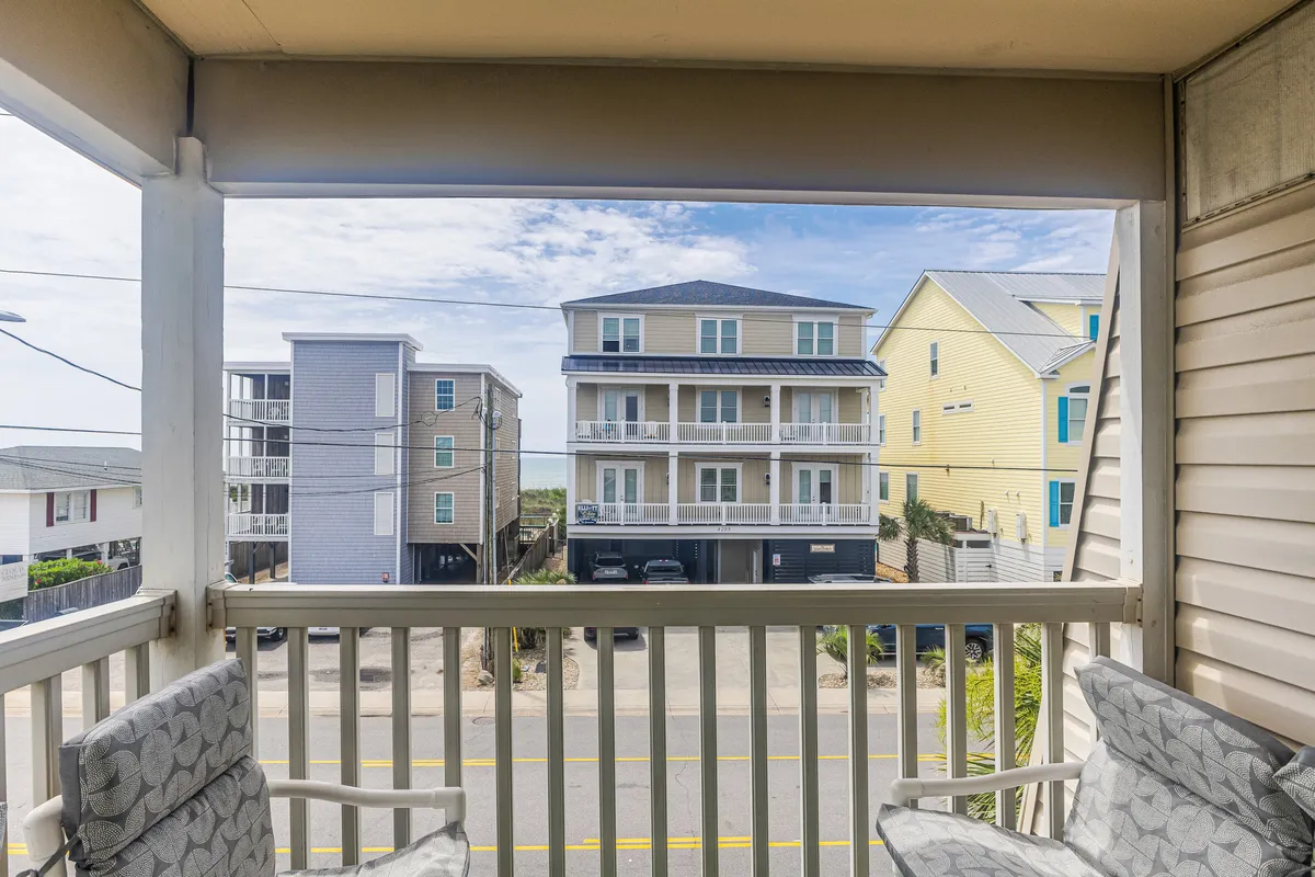 This image captures a tranquil balcony view overlooking the surrounding buildings and a vibrant street scene. The atmosphere suggests a laid-back community vibe, perfect for people-watching or relaxing with a morning coffee, and hints at the lively, social energy just outside the Groovy Surf Shack.