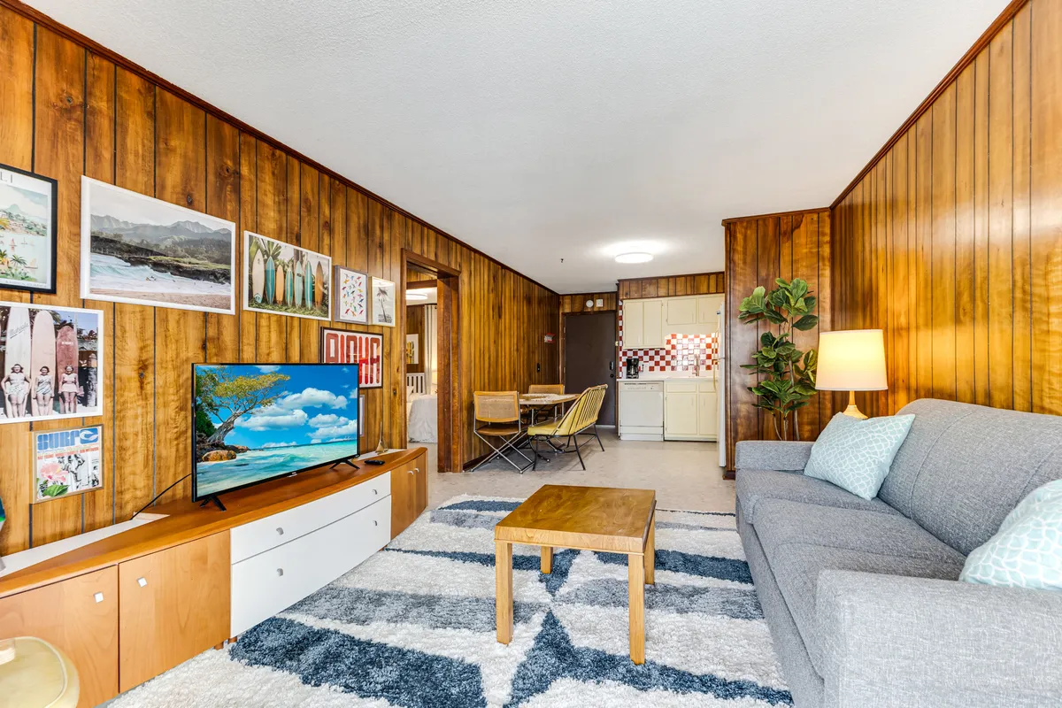 A welcoming living room with a modern gray sofa, a vibrant gallery wall filled with eclectic artwork, a wooden coffee table, and an indoor plant. The TV sits on a media console, making the space ideal for relaxing, socializing, or enjoying games and movies.