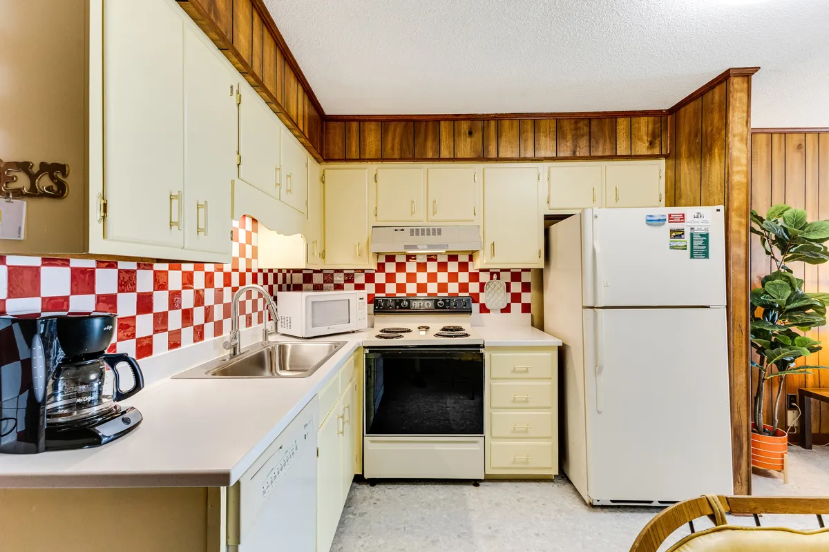 A nostalgic kitchenette with checkerboard backsplash, wood paneling, and a kitchen island. The appliances are visible, creating an inviting atmosphere for simple meal prep and casual gatherings.