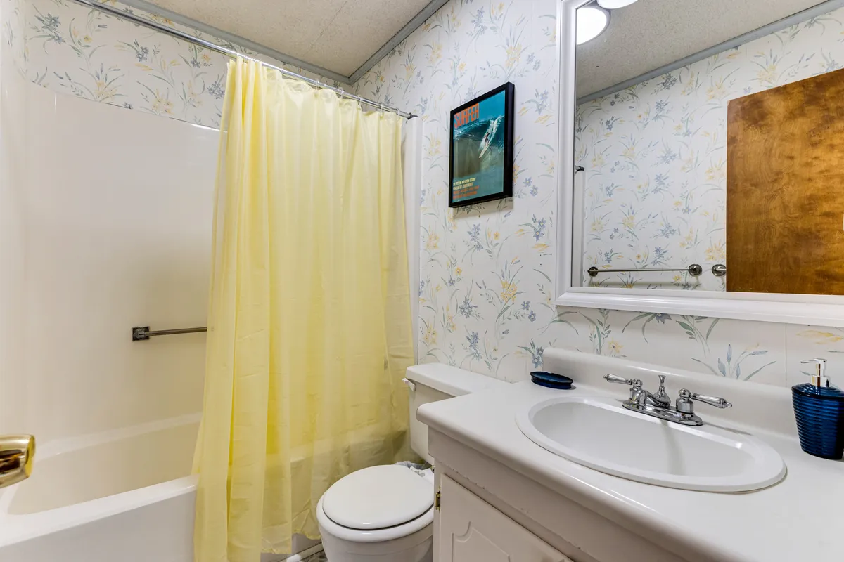 A cheerful, retro-inspired bathroom with a bold yellow shower curtain, floral wallpaper, and a classic sink vanity. A framed poster on the wall adds playful personality, while the space feels both bright and welcoming.